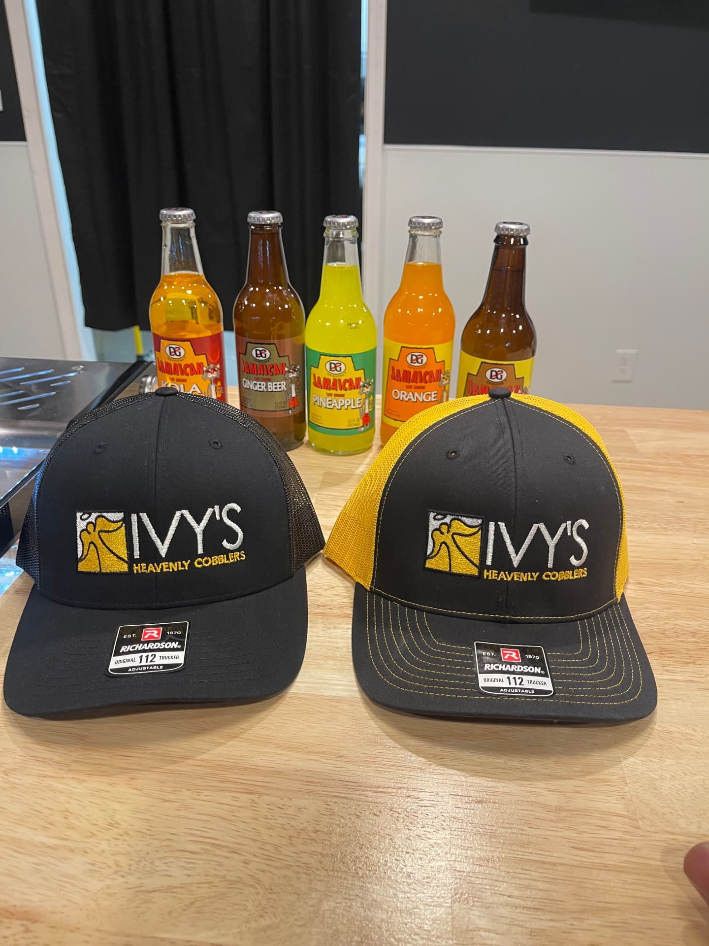 Ivy's Heavenly Cobblers branded trucker hats with Jamaican sodas on the counter